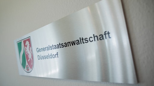 Ein Schild mit der Aufschrift "Genrealstaatsanwaltschaft Düsseldorf" und dem Wappen von NRW hängt an einer Wand.