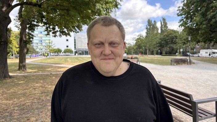 Ex-Häftling Manuel B. lächelt in die Kamera und steht vor einer Parkbank.
