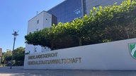 Ein halb graues und halb verglastes modernes Gebäude, davor ein Schild mit der Aufschrift "Oberlandesgericht Generalstaatsanwaltschaft".