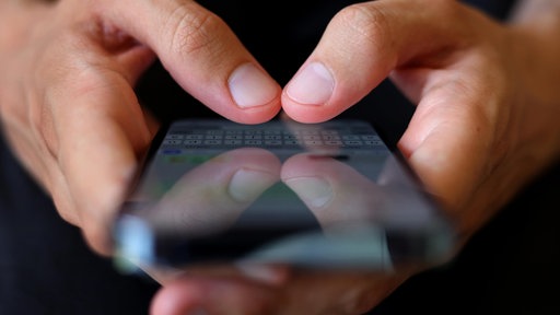 Auf dem Foto ist ein Smartphone, auf dem Finger etwas in einen Whatsapp-Chat tippen.