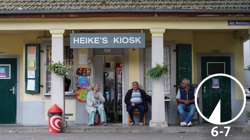 Drei Menschen sitzen vor dem hell-gestalteten Kiosk