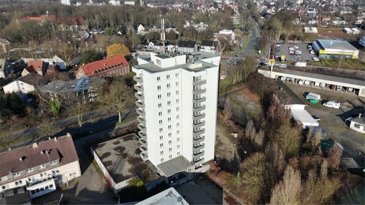 Ein helles Hochhaus umgeben von Gebäuden und Bäumen