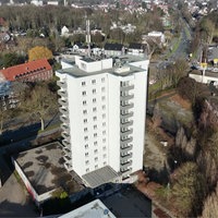 Ein helles Hochhaus umgeben von Gebäuden und Bäumen