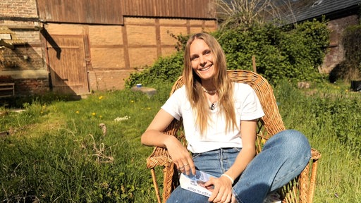 Leonie sitzt auf einem Stuhl im Garten und lacht in die Kamera.