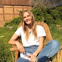 Leonie sitzt auf einem Stuhl im Garten und lacht in die Kamera.