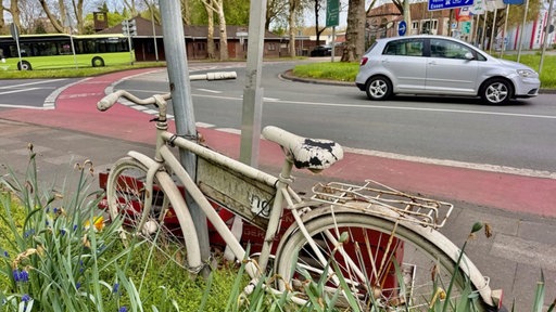 Ein altes, weiß angemaltes Fahrrad, im Hintergrund einen großen Kreisverkehr.