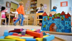 Eine Spielburg und Bauklötze, im Hintergrund unscharf mehrere Kinder in einer Kindergruppe