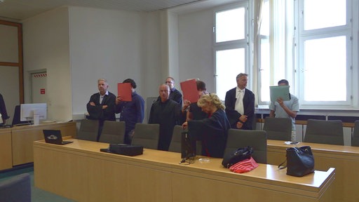 Vier angeklagte Männer halten sich im Gericht Mappen vor den Kopf