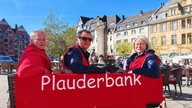 Drei Menschen sitzen auf einer Stadtbank