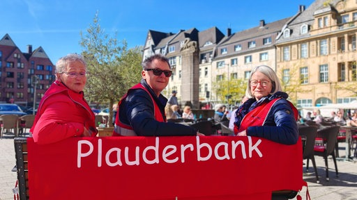 Drei Menschen sitzen auf einer Stadtbank