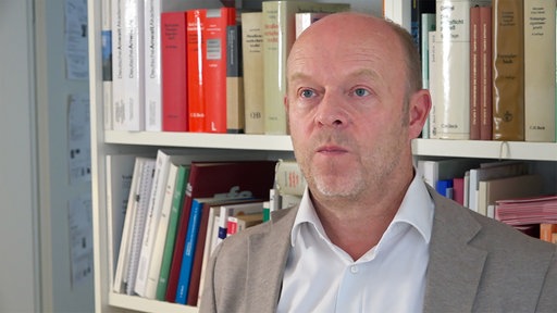 Rechtsanwalt Arndt Kempgens steht vor einem Bücherregal.