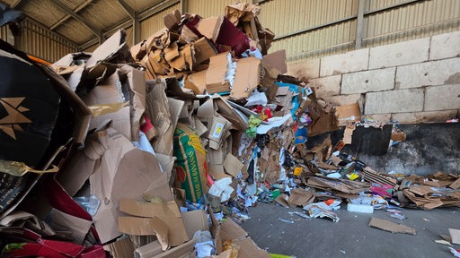 Ein großer Haufen Papiermüll liegt in einer Halle. Die Wand dahinter ist verrußt.