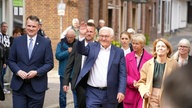 Frank-Walter Steinmeier geht einen Weg entlang, er hebt grüßend die Hand, neben ihm weitere Menschen