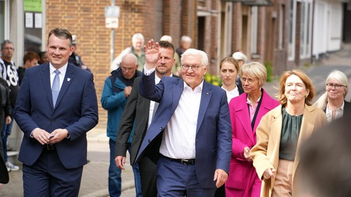 Frank-Walter Steinmeier geht einen Weg entlang, er hebt grüßend die Hand, neben ihm weitere Menschen