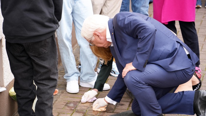 Frank-Walter Steinmeier und eine Schülerin knien am Boden und putzen Stolpersteine