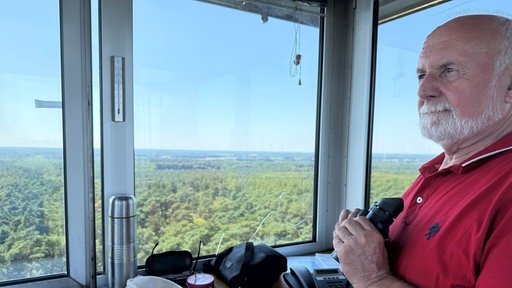 Ein Mann steht mit Fernglas in einem Wachturm