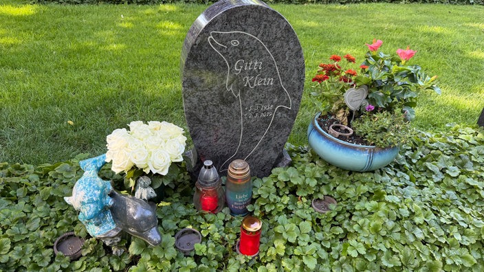 Ein Grabstein mit der Aufschrift Gitti Klein, davor Grablichter und Blumen.