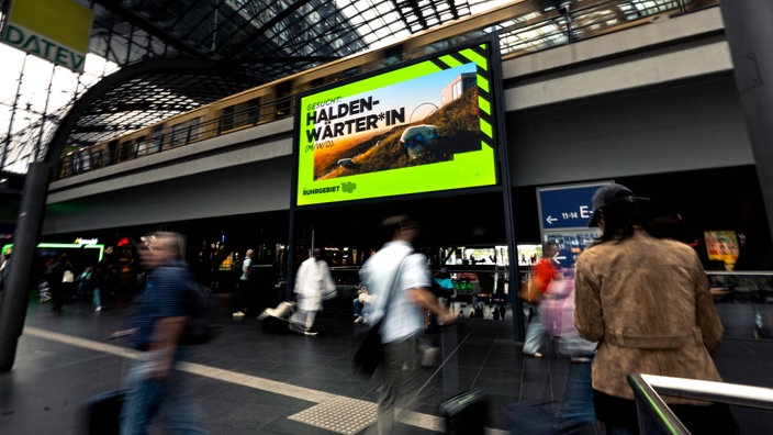 Im Berliner Hauptbahnhof läuft auf einer großen LED-Wand Werbung für die Suche nach dem Haldenwärter