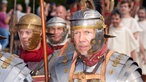 Ein Mann mit Helm und Rüstung steht inmitten anderer Männer. 