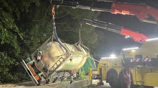 Zwei Kräne, die an einem verunfallten Lkw befestigt sind, richten das umgekippte Fahrzeug wieder auf. 