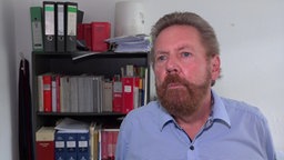 Anwalt Burkhard Kapteinat steht vor einem Regal voller Akten