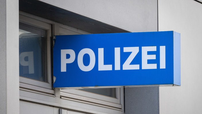 Blaues Polizeischild mit weißer Aufschrift „POLIZEI“ an der Fassade eines Gebäudes.