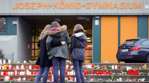 Drei Schülerinnen stehen vor zahlreichen Kerzen auf einer Treppe vor dem Schulgebäude 
