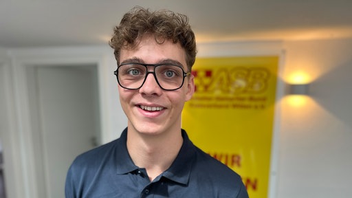 App-Programmierer Moritz Ulrich hat braune lockige Haare und trägt eine schwarze Doppelsteg-Brille. 