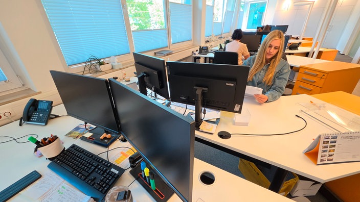 Eine blonde junge Frau sitzt in einem Büro am Schreibtisch.