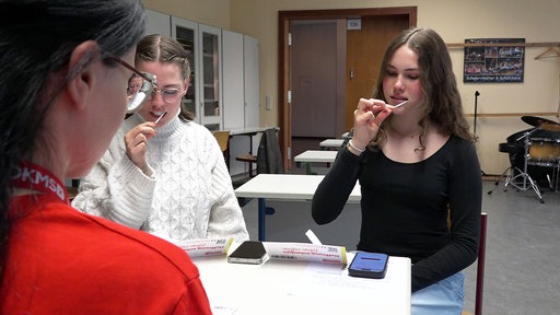 Noelia Telgmann und Hanna Knoblauch sitzen in einem Klassenraum und führen für die Typisierung jeweils ein Wattestäbchen durch ihren Mund.