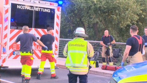 Mehrere Einsatzkräfte stehen vor einem Notarztwagen auf einer Brücke.
