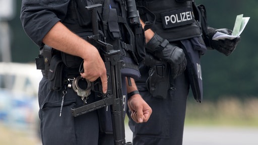 Zwei Polizeieinsatzkräfte von nahem, einer hält ein Maschinengewähr griffbereit.