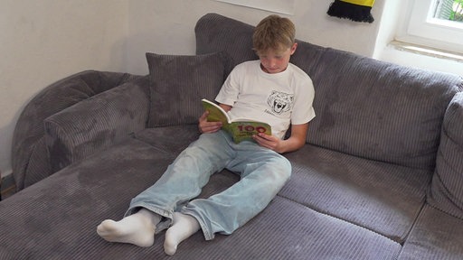 Benjah Müller, zehnjähriges Kind sitzt auf einer Couch und liest ein Buch.