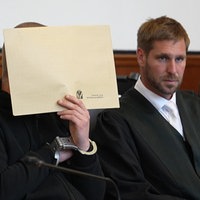 Der Angeklagte hält sich im Gerichtssaal eine Aktenmappe vors Gesicht