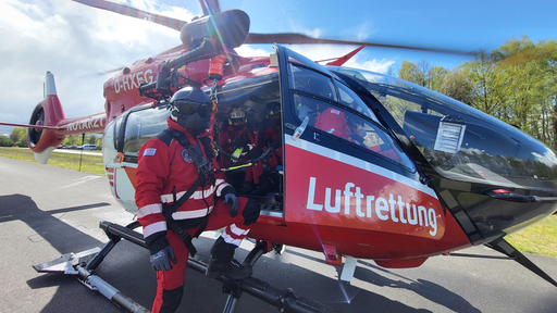 Ein Hubschrauberpilot steht vor einem roten Hubschrauber mit der Aufschrift Luftrettung