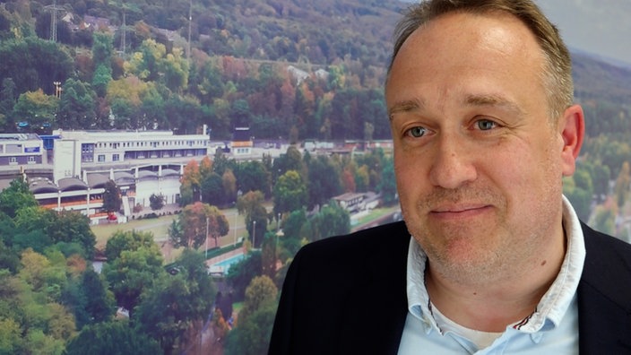 Dirk Broska spricht während eines Interviews. Im Hintergrund ist ein großformatiges Luftbild der Schauinsland-Reisen-Arena in Duisburg zu sehen.