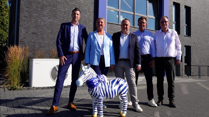 Dirk Broska, Veronika Henschel-Grontzki, Ralf Raddue, Dirk Recke und Thorsten Immel stehen gemeinsam mit einer blau-weißen Zebraskulptur vor einem Gebäude in Duisburg.