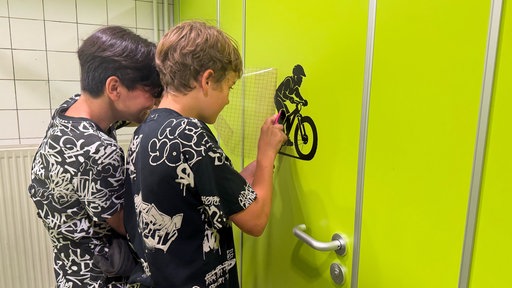 Zwei Jungen kleben Sticker auf eine Toilette