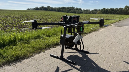 Eine Drohne steht am Boden vor einem Feld