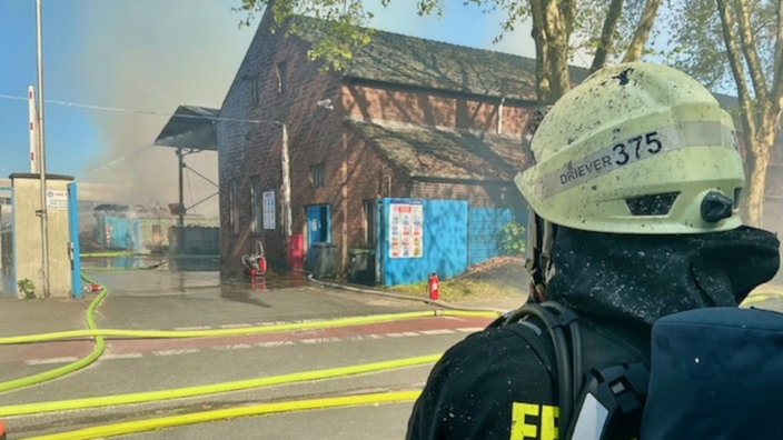 Ein Feuerwehrmann steht vor dem brennenden Recyclinghof in Mülheim