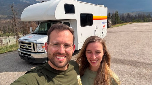 Alexandra und Lukas stehen vor einem Wohnmobil auf einer Straße.