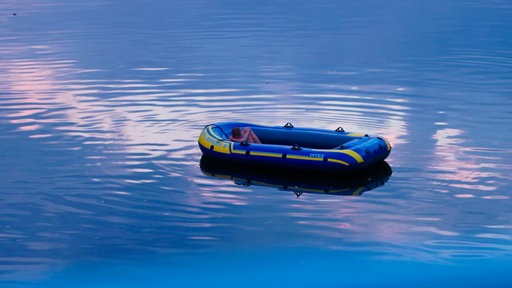 Ein Mann schläft in einem blau-gelben Schlauchboot auf der Ruhr