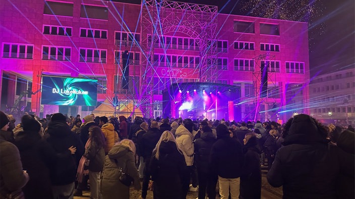 Das Rathaus der Stadt Dortmund wird lila angestrahlt. Davor stehen Menschen