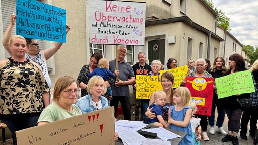 Protestierende Mieter stehen vor einem Wohnhaus und halten Plakate hoch