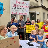Protestierende Mieter stehen vor einem Wohnhaus und halten Plakate hoch