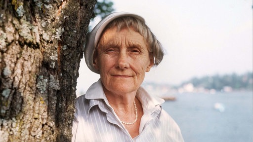 Astrid Lindgren steht an einem Baum gelehnt und schaut in die Kamera.