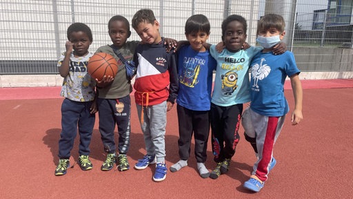 Amari steht zusammen mit fünf weiteren Freunden auf dem Fußballfeld im Friedensdorf Oberhausen.