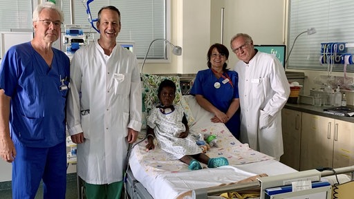 Amari im Krankenbett und die behandelnden Ärzte aus Leipzig nach der Operation im Krankenzimmer.