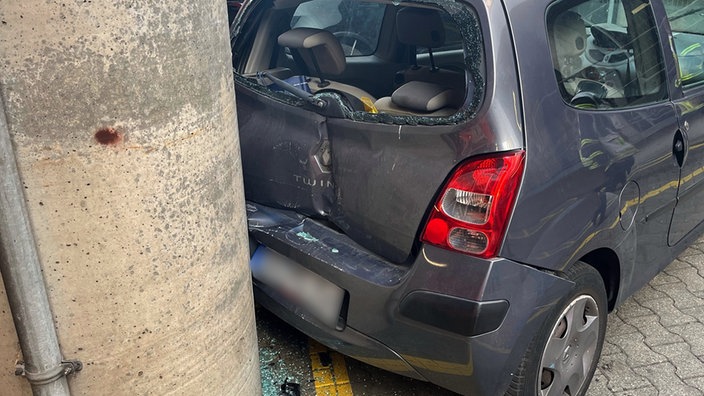 Ein beschädigter Renault Twingo steht mit eingedrücktem Heck an einer Betonsäule, die Heckscheibe ist zerstört und Glassplitter liegen auf dem Boden.