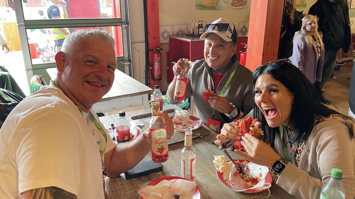 Kevin, Alicia und Christian sitzen an einem Tisch und essen Erdbeer-Döner
